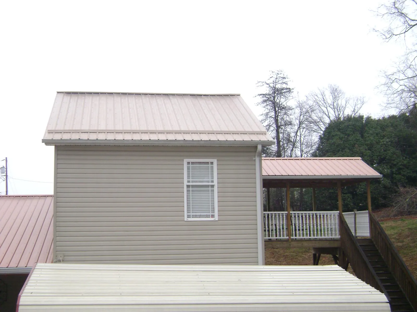 Tan metal roofs on a two story addition and attached porch, from a Roof Replacement job in Bainbridge